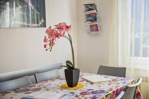 Et bord med dug med blomster, en vase med lyserøde blomster, en bog og et magasin på væggen.