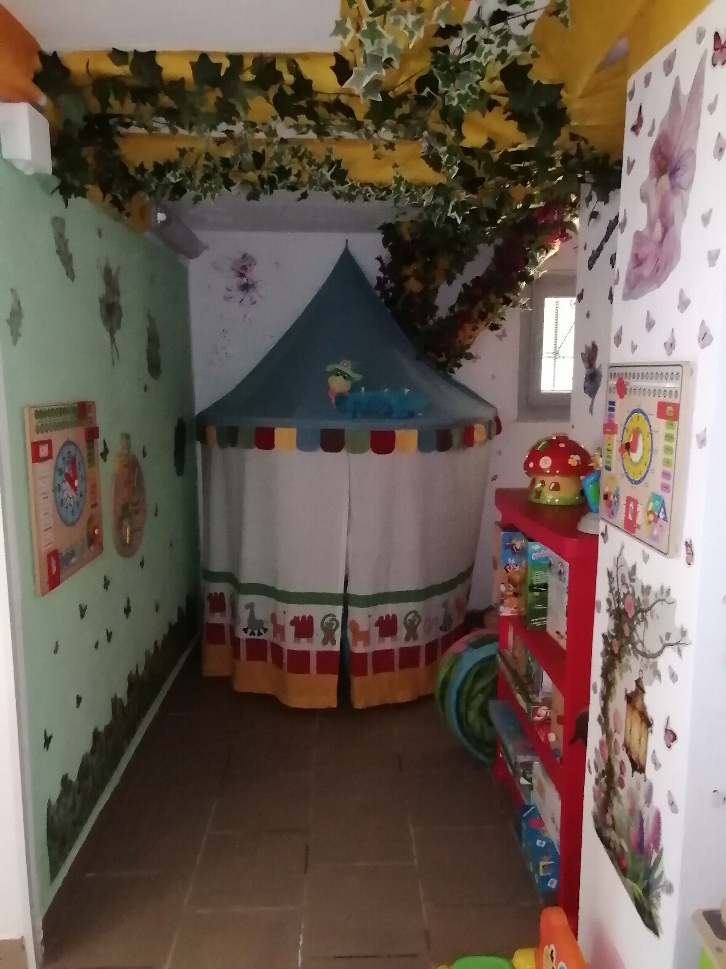 A child's playroom with a tent, educational wall decorations, and a shelf with toys.
