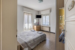 A bedroom with a bed, a dresser, a TV, and a window with curtains. - Casa Vacanza Elena: Family Paradise with Garden, Private Parking, Pet-Friendly, Val Grande View (Santino VB)