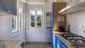 A kitchen with a gas stove, a window with curtains, a radiator, and a blue cabinet.
