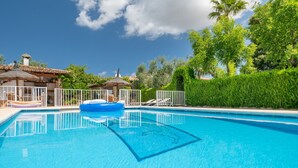 Uma piscina azul límpida com um flutuador, cercada por uma cerca branca, e um edifício com telhado telhado ao fundo.