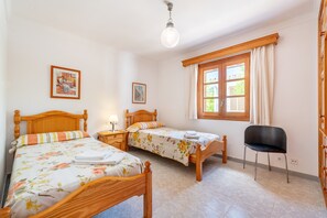 A bedroom with two wooden beds, a chair, a window with curtains, and a wall-mounted light fixture. - Villa la Rafal with Mountain View, Pool, Wi-Fi, A/C, Terrace & Garden (Pollensa)