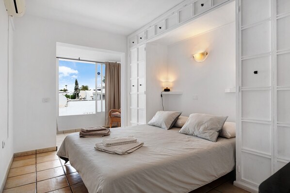 A bedroom with a bed, a window with curtains, a wall-mounted light, and a view of the outside.