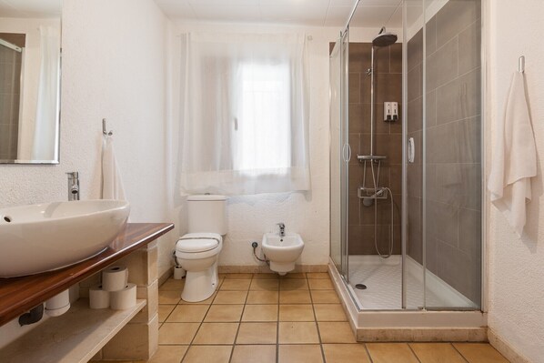 A bathroom with a large sink, toilet, bidet, and a glass-enclosed shower.