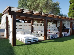Un espace extérieur abrité, doté de bancs et de tables en bois peints en blanc, et entouré d’une clôture blanche.