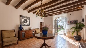 A room with a round wooden table, a blue vase, a sofa, a cabinet, and a chandelier. - Pet-Friendly Villa Masía Can Trabal with Mountain View, Pool, Jacuzzi, Wi-Fi, A/C, Terrace & Garden (Olèrdola)