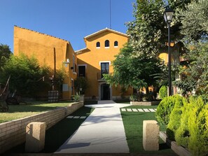 Une cour avec un chemin, un bâtiment à la façade jaune et de la verdure tout autour.