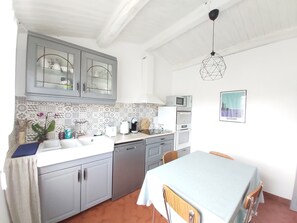 A kitchen with grey cabinets, a tiled backsplash, a microwave, an oven, and a dining area with a table and chairs.