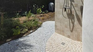 Ein Garten mit einem gefliesten Duschbereich, einem Kiesweg und einer Ziegelmauer.