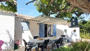 Eine Terrasse mit Tisch und Stühlen, einem hängenden Korb und einem kleinen Garten mit weißen Blüten.
