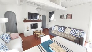 Ein geräumiges Wohnzimmer mit Kamin, einer Sofagarnitur, einem Couchtisch und einem an der Wand montierten Fernseher.