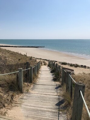 Ein hölzerner Steg führt zu einem Strand, begrenzt auf einer Seite von einem Holzzaun und auf der anderen Seite von einem hölzernen Steg.