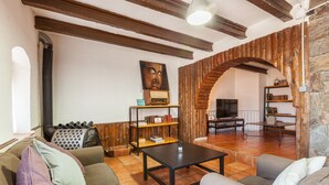 Un salon comprenant un canapé, une table basse, une bibliothèque, un téléviseur et un mur en pierre.