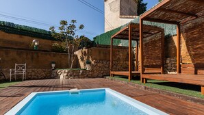 Une piscine dotée d’une terrasse en bois, d’un mur en pierre et d’une structure en forme de pergola.