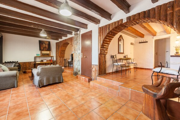 A spacious living area with a fireplace, wooden beams, and a stone wall.