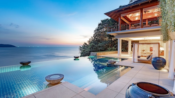 Une piscine à débordement luxueuse offrant une vue dégagée sur la mer, une terrasse en bois et un espace extérieur aménagé avec un éclairage soigné.