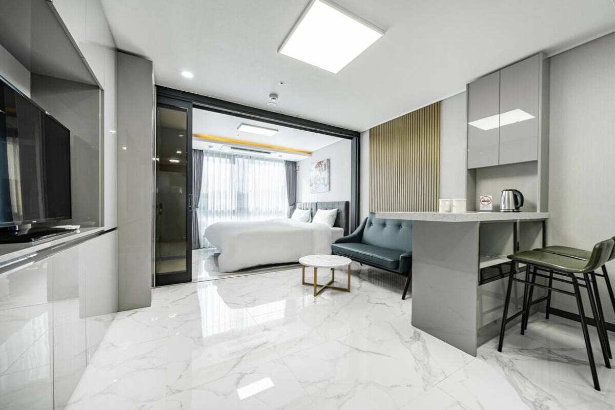 A modern hotel room with a bed, a sofa, a small table, and a TV.