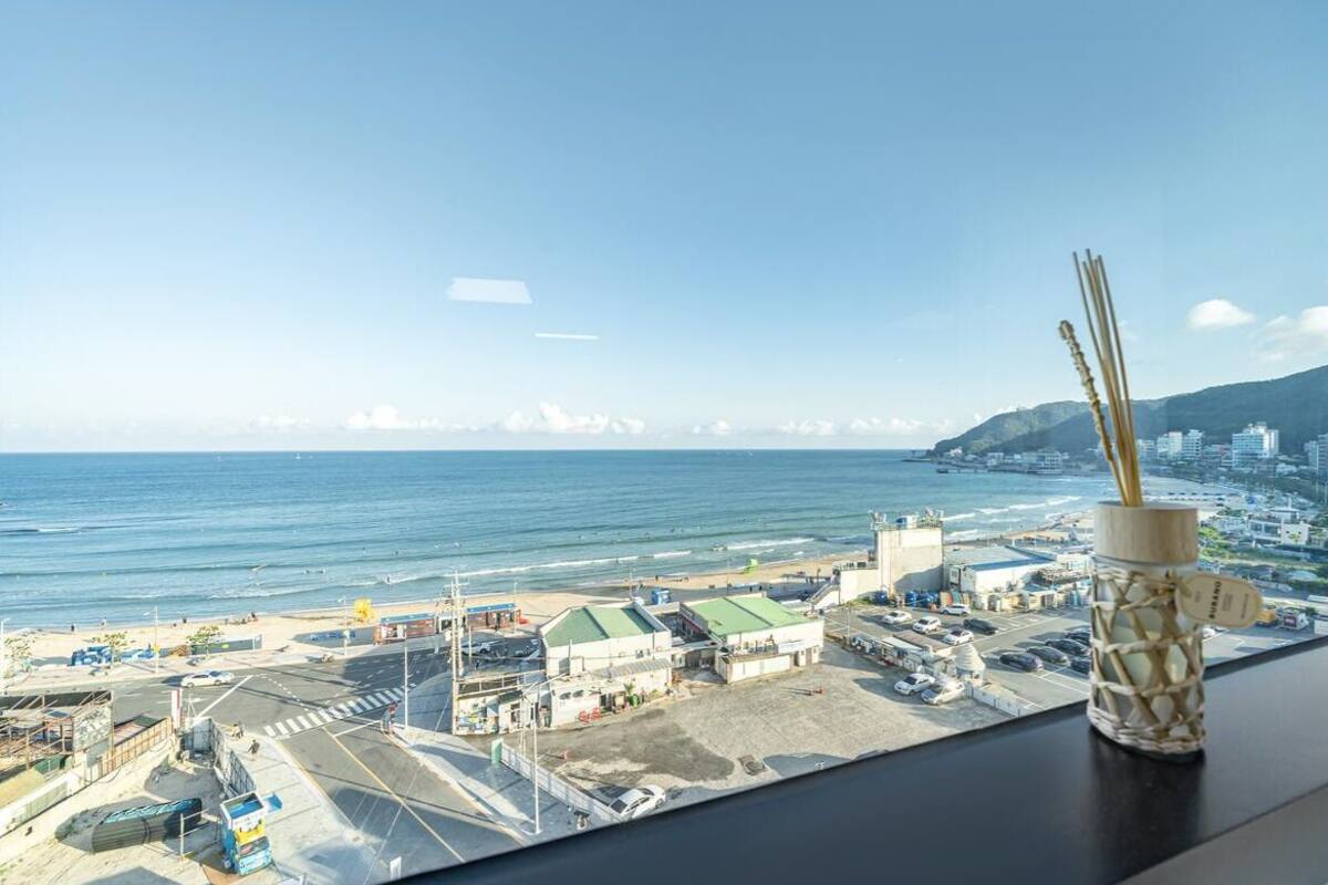 A view from a window overlooking a beach with a parking lot and buildings in the background.
