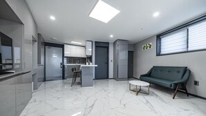 Una cocina moderna con piso de mármol, un comedor con sofá y una mesita, y un divisor corredizo que da a un balcón.