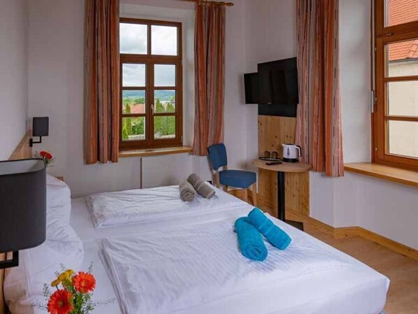 A hotel room with a bed, a desk, a chair, a television, and a window with a view. - Doppelzimmer DZ - Haus Weyregg - Frühstückspension (Weyregg am Attersee)
