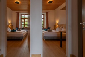 Une vue en miroir d’une chambre d’hôtel avec un plafond en bois, de grandes fenêtres avec des rideaux, un lit avec des oreillers et une couverture, une table de chevet avec une lampe et un plancher en bois.