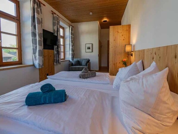A hotel room with two beds, a television, a sofa, and a wooden ceiling.
