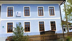 Un edificio de dos pisos con fachada azul claro, varias ventanas y una cerca de madera al frente.