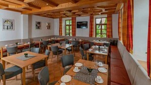 Un comedor con mesas y sillas de madera, un ventanal con cortinas y un televisor en la pared.