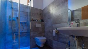 Un baño con ducha envuelta en vidrio, inodoro, lavamanos con espejo y toallero.