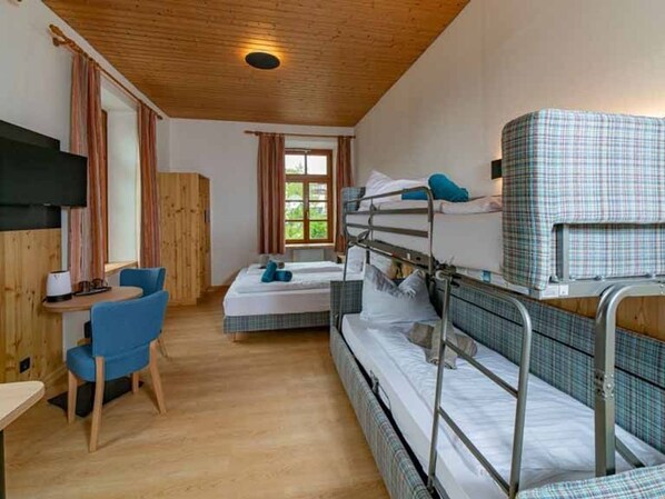 A bunk bed room with a desk and chair, a window with curtains, and a television on the wall.