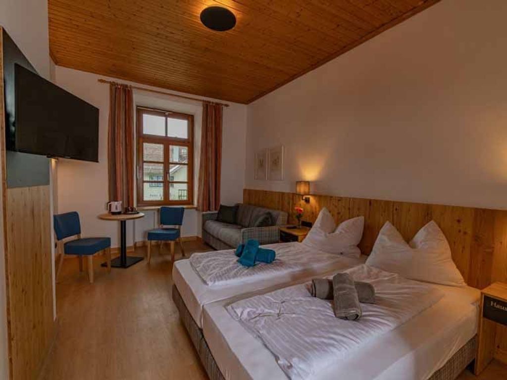 A hotel room with two beds, a TV, a small table, and a window with curtains.