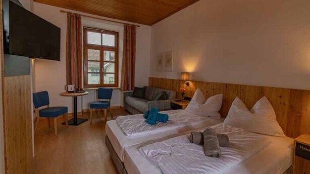 Quarto de hotel com duas camas, televisão, uma mesinha e janela com cortinas.
