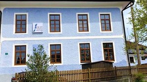 A two-story building with a light blue exterior, multiple windows, and a wooden fence in front.
