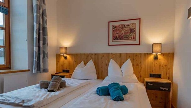 A hotel room with two beds, a wooden headboard, wall-mounted lamps, and a framed picture on the wall. - Junior Suite JS - Haus Weyregg - Frühstückspension (Weyregg am Attersee)
