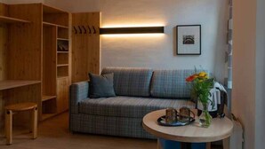Ein gemütliches Zimmer mit einem karoüberzogenen Sofa, einem Holzschrank, einem kleinen Tisch mit Tablett und einer wandmontierten Lampe.