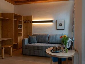 Una habitación acogedora con un sofá a cuadros, un armario de madera, una mesita con una bandeja y una lámpara de pared.