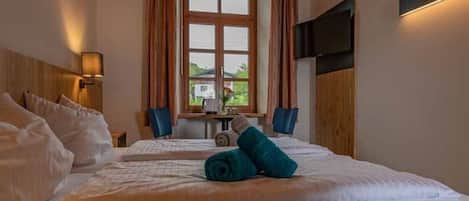 Habitación de hotel con cama, televisor montado en la pared, ventana con cortinas y vistas al exterior.