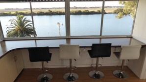 Una habitación con tres taburetes y un amplio ventanal con vista al agua y vegetación.