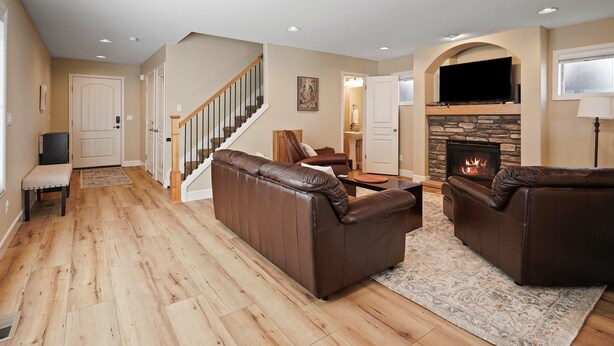 A spacious living room with a fireplace, leather sofas, a wooden floor, and a staircase.