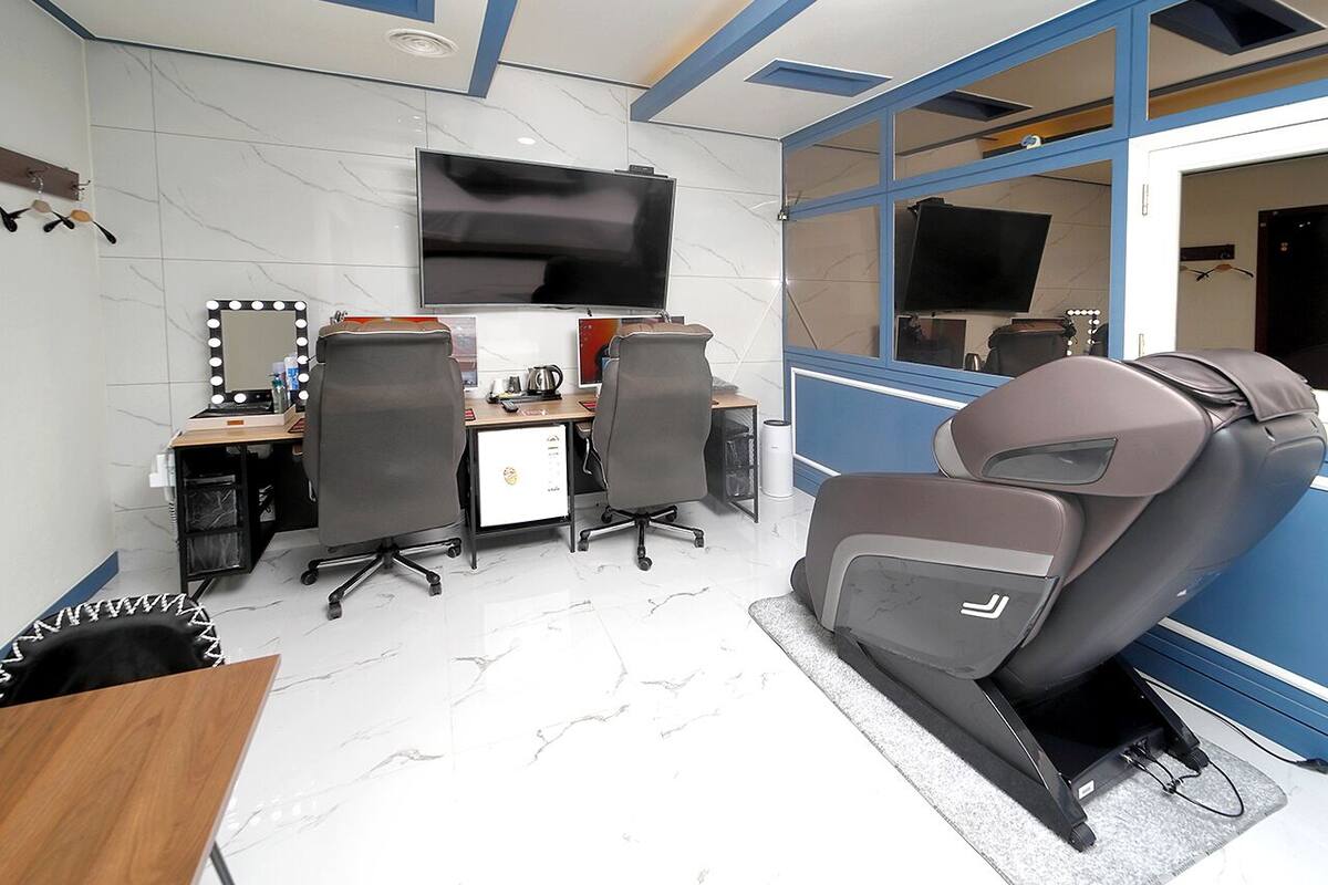 A modern room with a massage chair, a desk with a computer, and a TV.