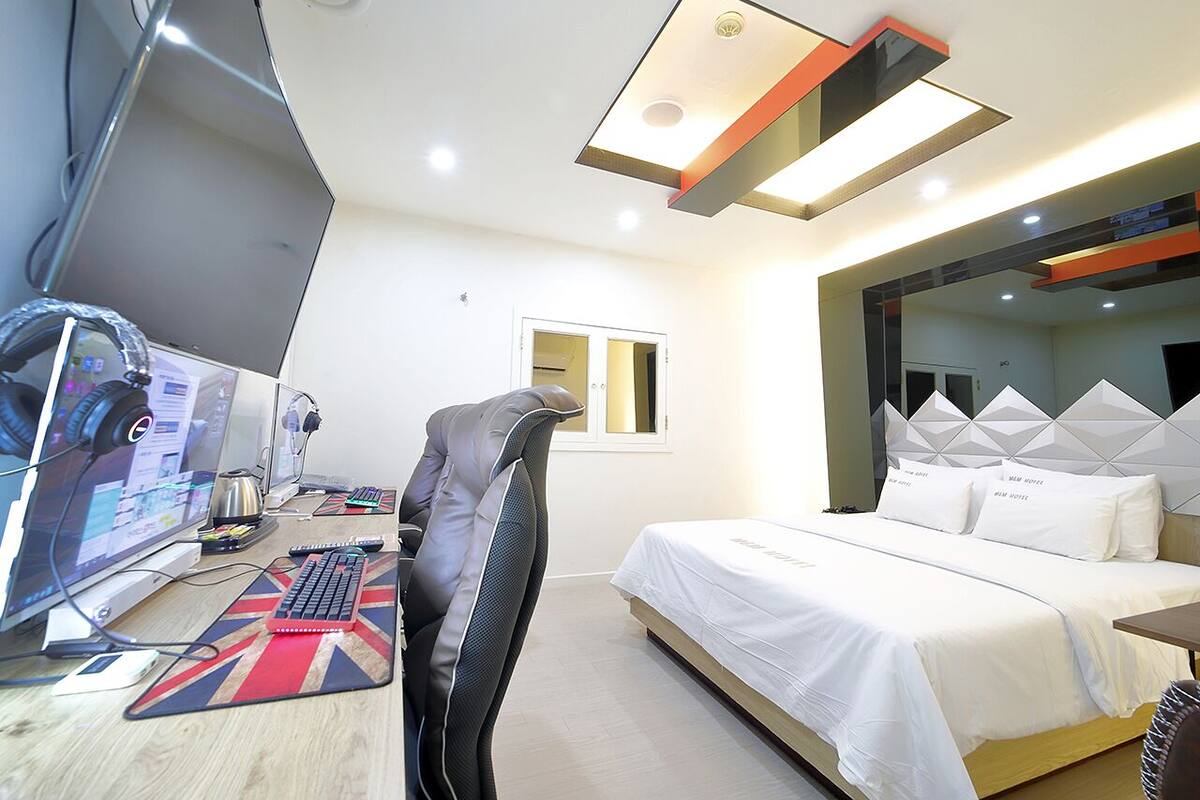 A modern hotel room with a bed, desk, computer, and a massage chair.
