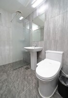 Un baño moderno con ducha, lavamanos, inodoro y un espejo grande.