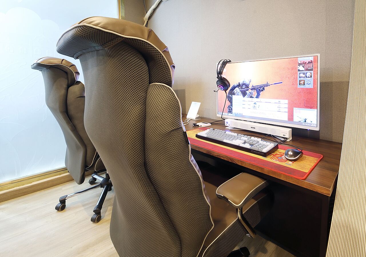A modern office chair with wheels, a desk with a computer setup, and a window with blinds.