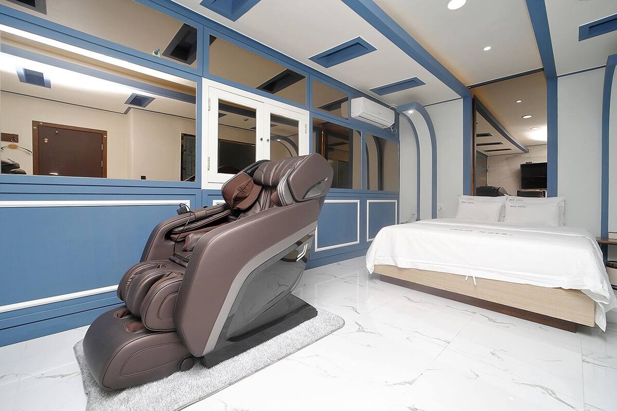 A modern bedroom with a massage chair, a bed, and a large mirror.