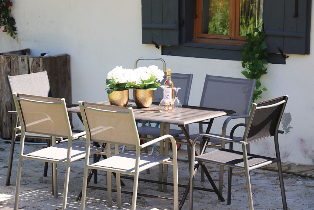 Ein Tisch im Freien mit sechs Stühlen, einer Blumenvase und einer Flasche.