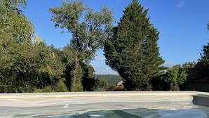A swimming pool with clear water, surrounded by trees and a house in the background. - La maison d’Etang (Saint-Paul-la-Roche)