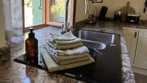 A kitchen with a sink, a bottle, and a stack of towels. - La maison d’Etang (Saint-Paul-la-Roche)