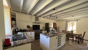 A spacious kitchen with a central island, built-in appliances, and a dining area with wooden furniture. - La maison d’Etang (Saint-Paul-la-Roche)