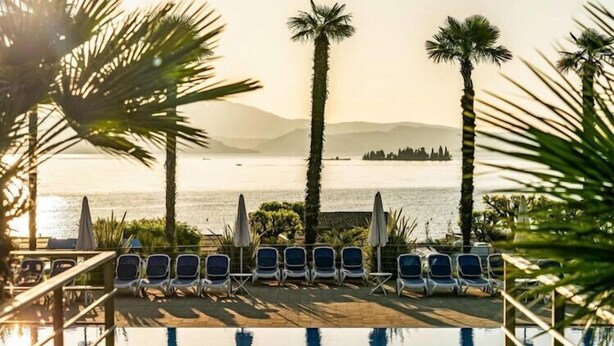 A poolside area with lounge chairs and umbrellas, overlooking a body of water and distant land.