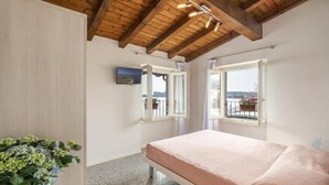 A bedroom with a wooden ceiling, a bed, a window with a view, and a plant.